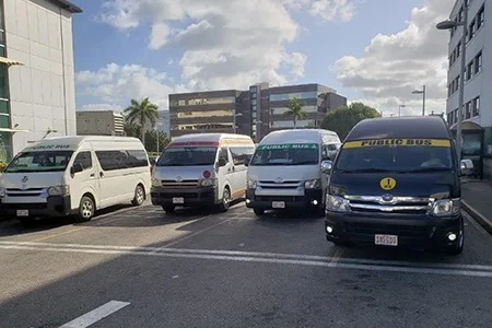 Four passenger vans marked PUBLIC BUS across the windscreen, parked in a row at the George Town bus depot.